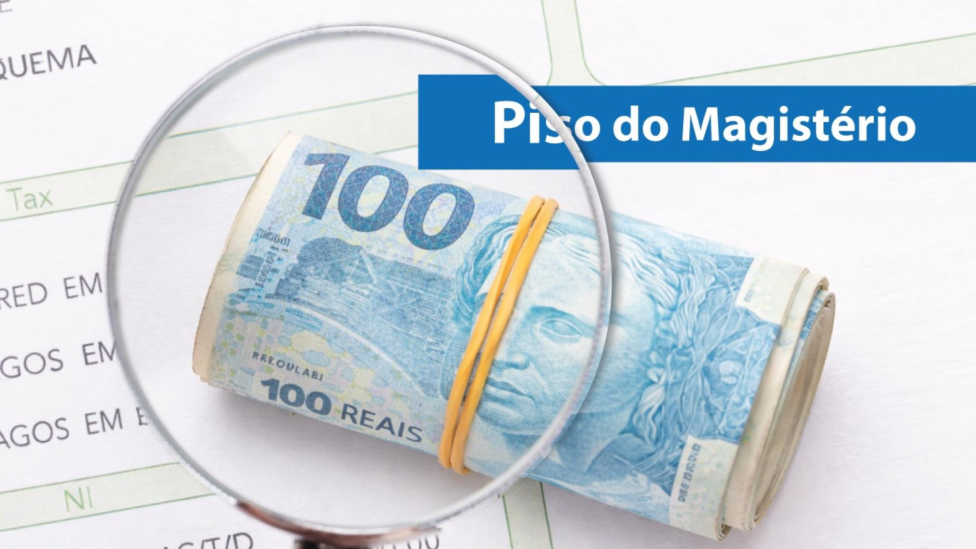 Banner horizontal com foto mostrando cédulas de 100 reais enroladas e presas com elástico amarelo, posicionada sobre documentos com textos parcialmente visíveis. Uma lupa amplia a área da cédula. No canto superior direito, há faixa azul com o texto “Piso do Magistério”.