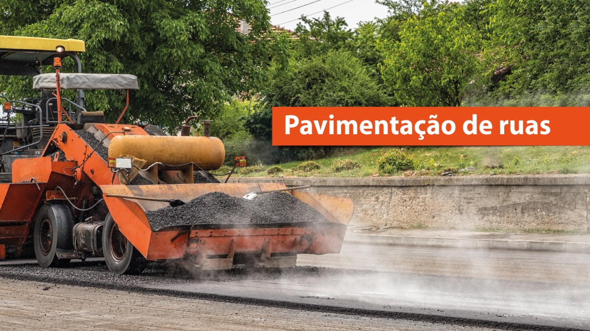 Banner horizontal com imagem de obra de pavimentação urbana. À esquerda, aparece uma máquina pavimentadora em operação, aplicando material sobre a via, com liberação de vapor durante o processo. Ao fundo, há vegetação e árvores. À direita da imagem, faixa vermelha com o texto “Pavimentação de ruas”.