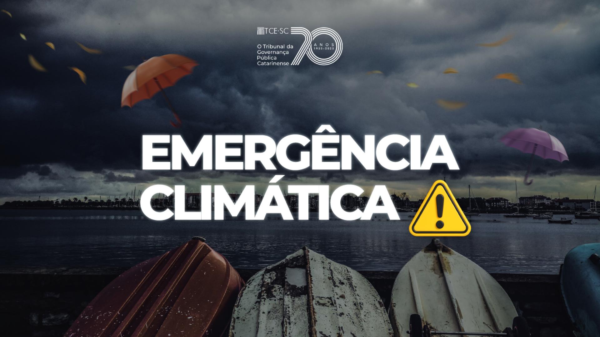 Banner horizontal com foto de paisagem costeira sob um céu escuro e carregado por nuvens de tempestade. No primeiro plano, há pequenos barcos virados de cabeça para baixo alinhados à beira da água. Aparecem guarda-chuvas coloridos sendo levados pelo vento e folhas espalhadas pelo ar, sugerindo condições climáticas extremas. Sobre a imagem, em fonte branca, o texto "Emergência climática", ao lado de ícone de atenção amarelo.