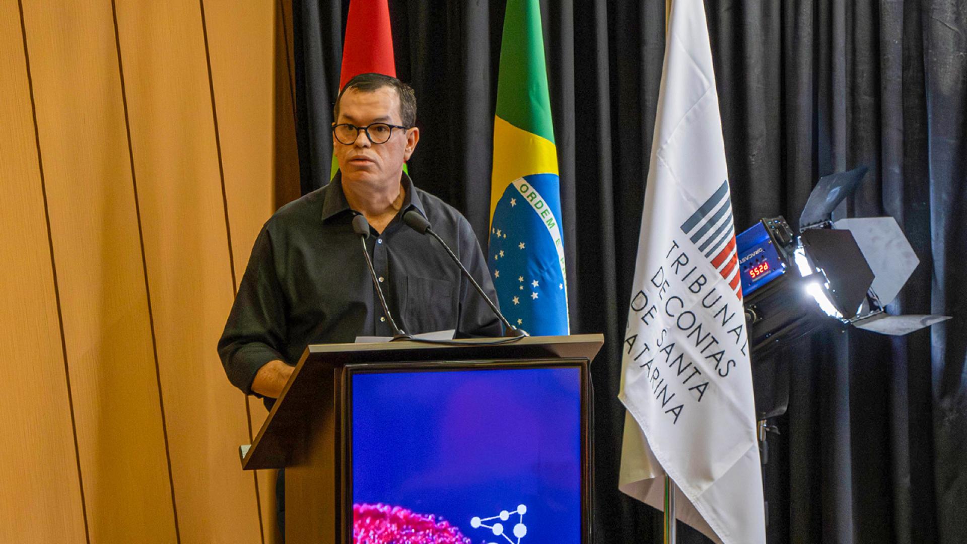 Foto do conselheiro Adircélio de Moraes Ferreira Júnior falando do púlpito. Atrás dele as bandeiras de Santa Catarina, do Brasil e do TCE/SC.