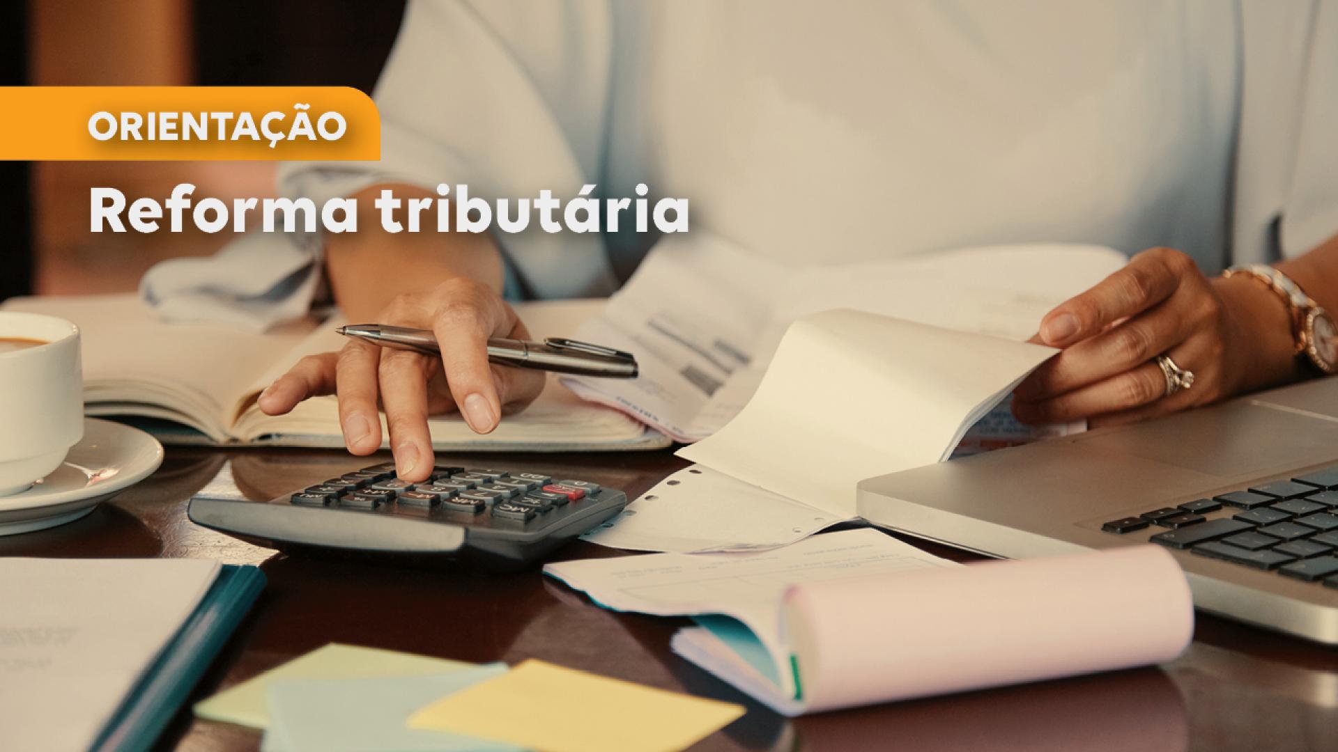 Banner horizontal com foto de uma mulher mexendo em vários papéis, calculadora e notebook, dispostos sobre uma mesa. A foto está cortada, de modo que só é possível ver as suas mãos. Sobre a imagem, à esquerda, em laranja e branco, o texto “Orientação. Reforma tributária”. 