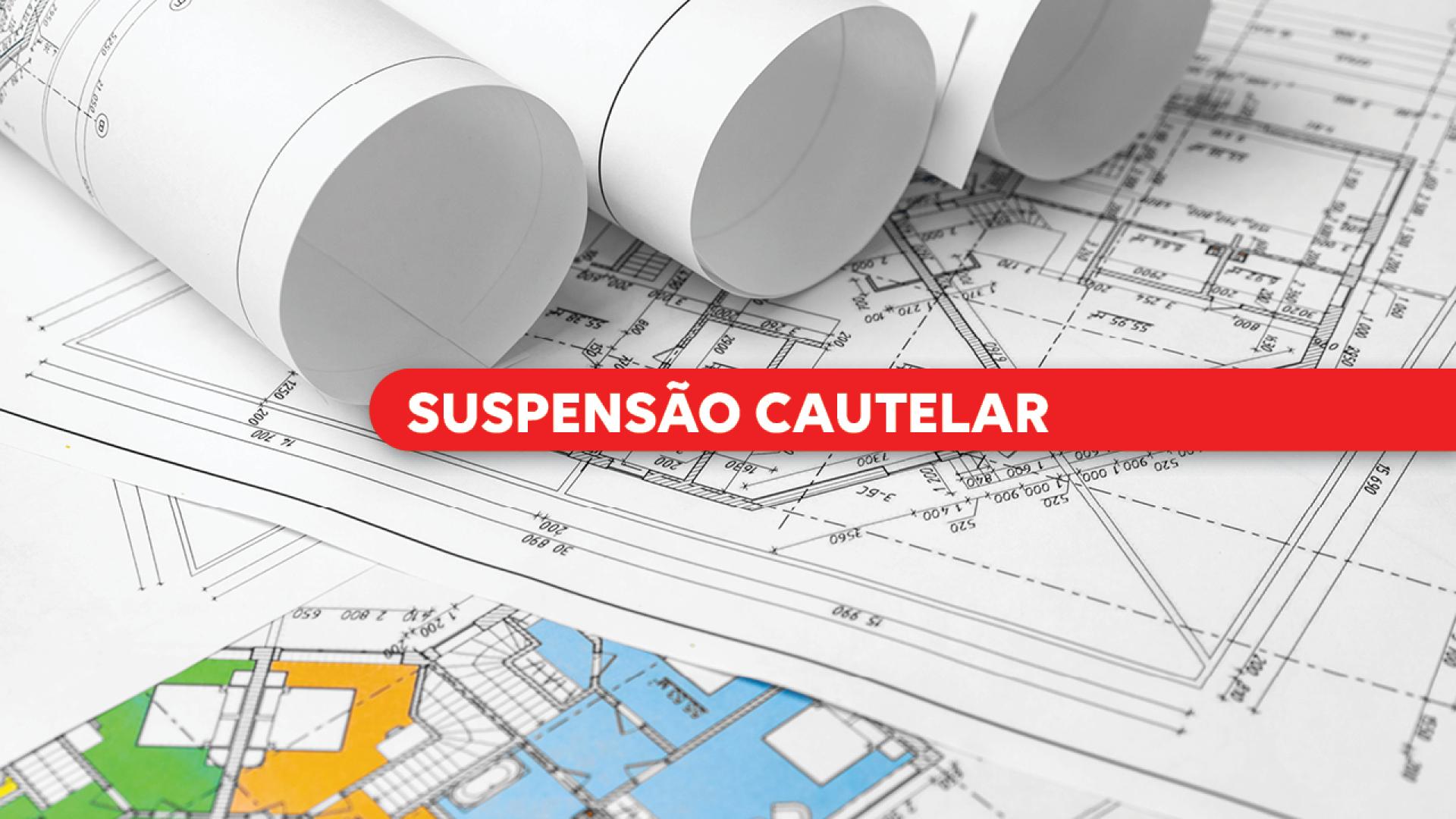 Imagem mostra projetos de arquitetura e engenharia sobre uma mesa. Do centro para a direita, sobre uma tarja vermelha, está escrito "suspensão cautelar" em letras brancas