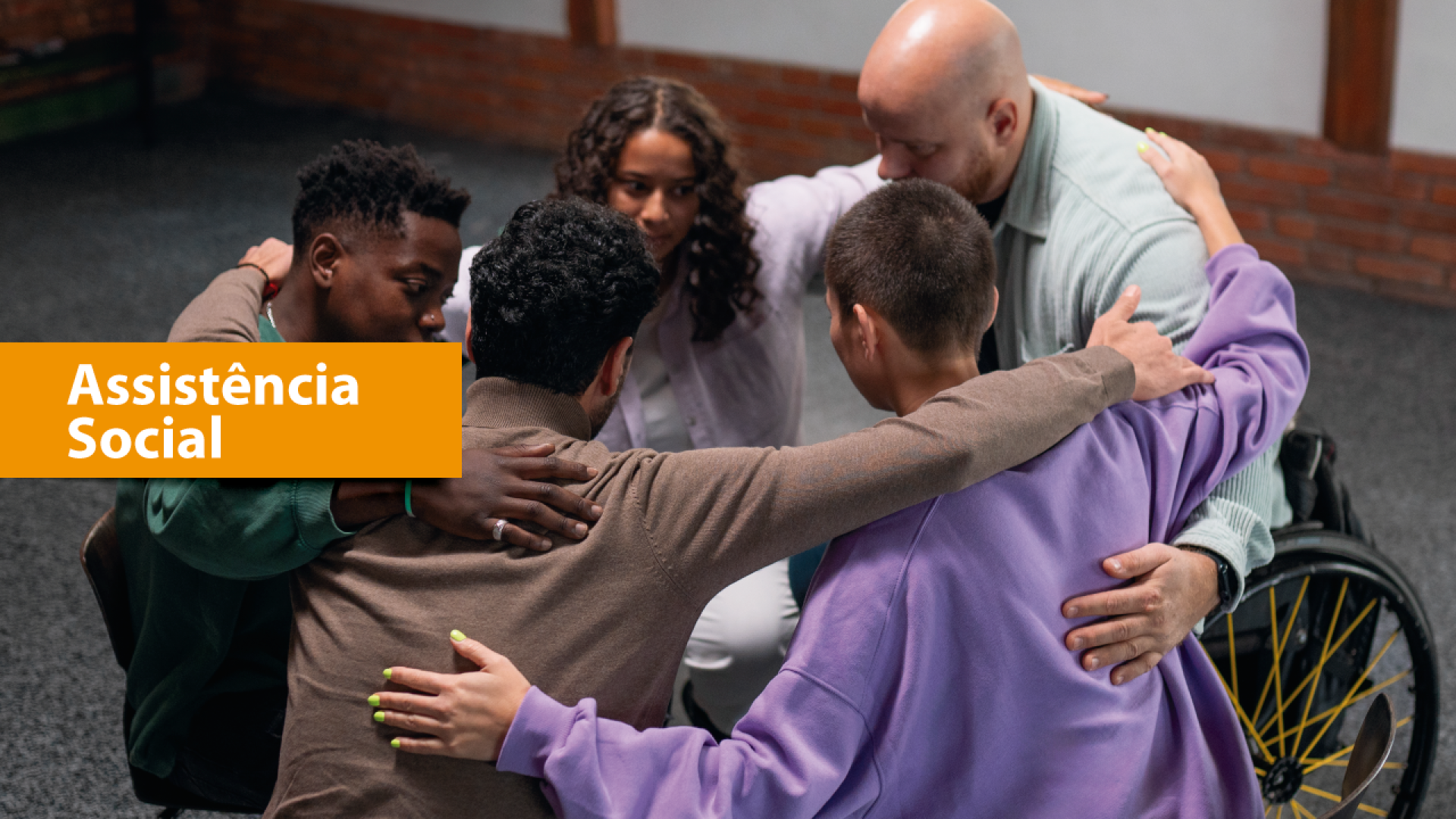 Imagem mostra cinco pessoas se abraçando, uma delas em cadeira de rodas. À esquerda, escrito em branco sobre tarja amarela, há a expressão Assistência Social. 