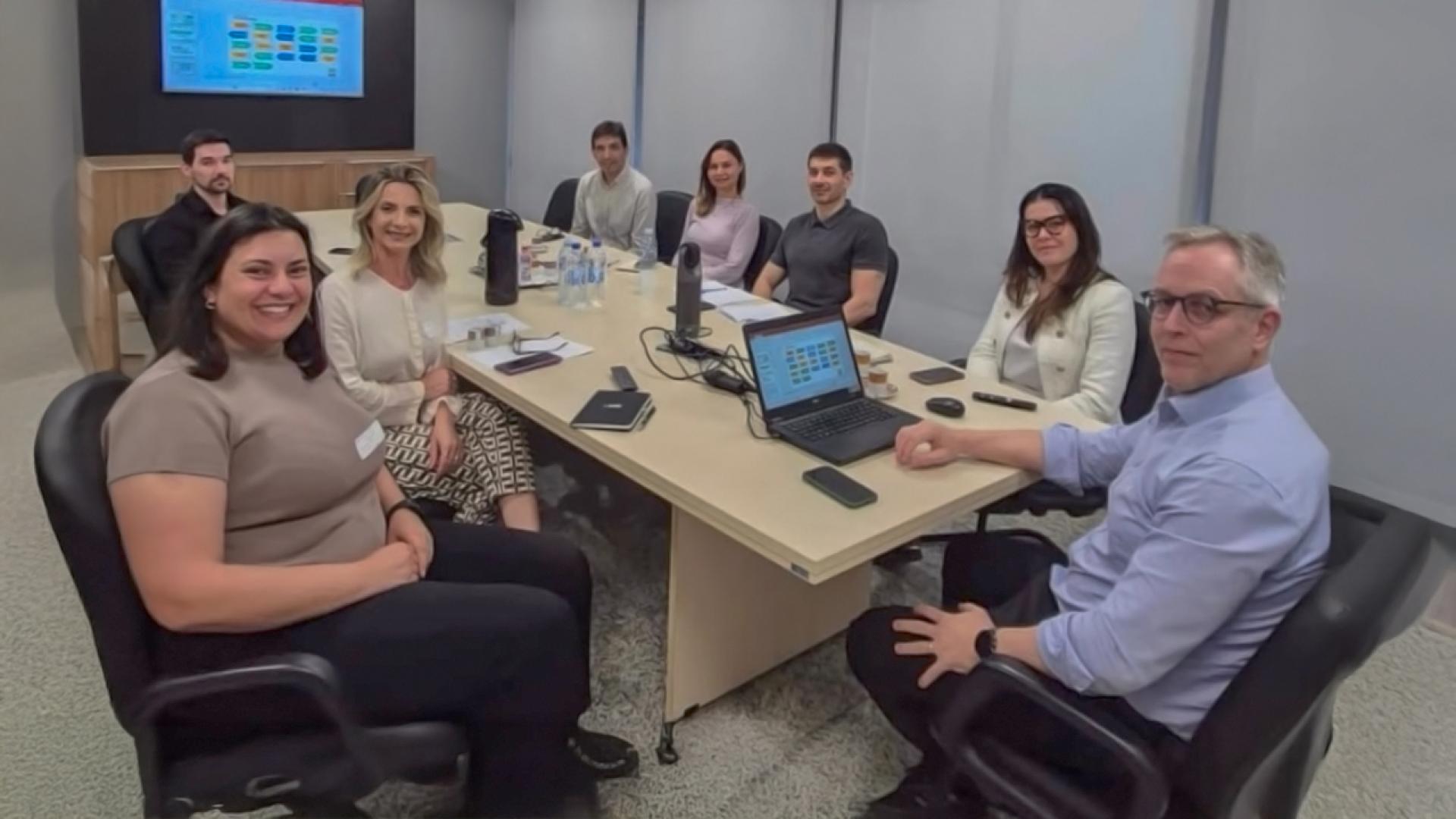 Banner horizontal com foto de várias pessoas sentadas ao redor de uma mesa de reuniões. Todos olham para a câmera. Entre os presentes, os auditores do TCE/SC Sidney Tavares Junior, Monique Portella, Francielly Coelho e Rogério Loch. Sobre a mesa, há notebook, celulares, garrafas e agendas. 