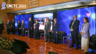 Foto com as 10 autoridades — nove homens e uma mulher — que participaram da solenidade de abertura do 1º Congresso Nacional de Comunicação dos Tribunais de Contas. Elas estão em pé, no palco do auditório, e em frente a um painel de led. No canto superior esquerdo, o logotipo do evento. 