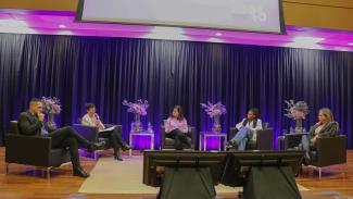 Foto de cinco pessoas no palco do TCE/SC durante roda de conversa realizada em alusão ao Agosto Lilás. São dois homens e três mulheres. Todos estão sentados em poltronas, um ao lado do outro. No cenário, há vasos de flores.