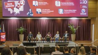 Foto do palco do TCE/SC, com os quatro palestrantes e ao centro, a diretora da Ouvidoria do TCE/SC, Walkiria Machado Rodrigues Maciel. ao fundo, o banner do evento.