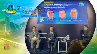 Banner horizontal. Ao fundo, com filtro em tons de azul, amarelo e verde, foto em marca d’água de Balneário Camboriú. Sobre a foto, ao centro, em um círculo, foto da participação do conselheiro Adircélio e do auditor Lucas no evento. Eles estão sentados, um ao lado do outro e ao lado do mediador. Usam fones de ouvido. Acima e atrás deles, um telão projeta a apresentação. No canto superior esquerdo, da imagem, logo do 21º Congresso Brasileiro de Contabilidade, e, no canto inferior esquerdo, logo do TCE/SC. 