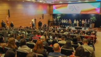 Em primeiro plano, de costas, há vários participantes sentados em poltronas no auditório do TCE/SC, durante a última etapa do Ciclo de Estudos. Em pé, no palco, ao fundo, estão os membros do TCE/SC que falam durante a abertura. Entre os presentes, os conselheiros Adircélio de Moraes Ferreira Júnior e Aderson Flores e o diretor do Icon, Moisés Hoegenn. 