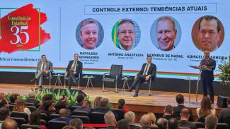 Banner horizontal com foto, em primeiro plano, da plateia que assiste ao painel “controle externo: tendências atuais”. À frente do público, no palco, os conselheiros Adircélio de Moraes e Herneus De Nadal, o deputado Napoleão Bernardes e o ministro do TCU Antônio Anastasia. Atrás deles, é projetado o título do painel e a foto dos participantes. 