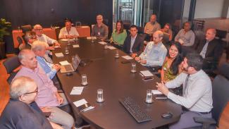 Foto horizontal com o conselheiro Wilson Wan-Dall e com servidores do TCE/SC e do TCE/PR — ao todo, há 16 pessoas, sendo 5 mulheres e 11 homens. A maioria está sentada em volta de uma mesa de reuniões. Sobre a mesa, há copos, papéis, canetas e equipamentos de informática. 
