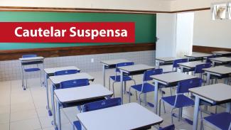 Banner horizontal com imagem de uma sala de aula com carteiras enfileiradas e vazias. Ao fundo, um quadro de giz. Sobre a foto, em tarja vermelha, o texto "Cautelar suspensa". 
