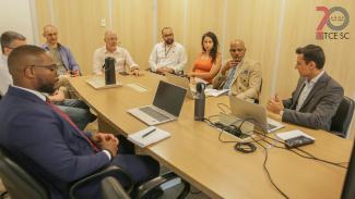 oto que mostra oito pessoas em volta de uma mesa, durante reunião. Entre os presentes, os visitantes do Tribunal de Contas de Angola e servidores do TCE/SC. Entre eles, Rafael Gonçalves e Jairo Wensing. No canto superior direito, logo do TCE/SC. 