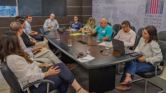 Banner horizontal com foto dos participantes da reunião. Há onze pessoas sentadas diante de uma mesa, enquanto conversam. Entre os presentes, o conselheiro substituto Gerson Sicca, integrantes da SED e do CAE. 