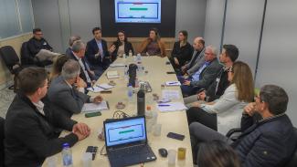 Banner horizontal com foto de várias pessoas sentadas ao redor de uma mesa de reuniões. Entre os presentes, representantes das associações de municípios e diretores do TCE/SC.