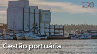 Imagem de área portuária vista a partir da água. Em primeiro plano, aparecem embarcações atracadas junto a um complexo industrial de grande porte, com estruturas de armazenamento e operação portuária. Na parte inferior da imagem, destaca-se o texto “Gestão portuária”.