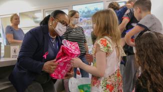 anner com foto de uma colaboradora do TCE/SC entregando um pacote de presente rosa a uma menina no Hospital Infantil. Em volta delas, há outras crianças recebendo presentes.