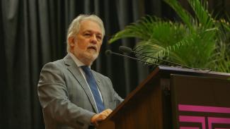 Banner horizontal com foto do desembargador João Henrique Blasi falando ao púlpito no auditório do TCE/SC, durante palestra. Ele é um homem branco, de cabelos e barba grisalhos. Veste terno e gravata.  