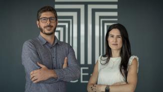 Banner horizontal com foto que mostra os auditores fiscais de controle externo Leandro Marques e Juliana Medeiros das Neves Moser, um ao lado do outro, em pé, com os braços cruzados. Leandro é um homem branco, de cabelos e barba escuros. Veste uma camisa azul e usa óculos de grau. Juliana é uma mulher branca, de cabelos compridos e castanhos. Veste roupa branca. Atrás deles, há uma parede cinza com o logo do TCE/SC na cor branca. 