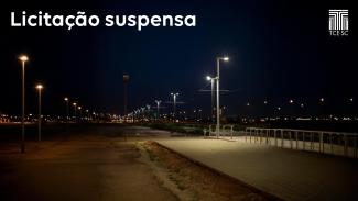 Foto noturna de uma ruma iluminada por vários postes. Na parte superior esquerda está o texto "Licitação suspensa", em letras brancas. E no canto superior direito, a logo do TCE/SC, também em branco.