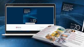 Banner horizontal com fundo azul-escuro. Ao centro, há um notebook e dois exemplares do livro de 70 anos, um aberto e um fechado, com páginas da publicação à mostra. A capa é azul-escuro, composta pelo título e pelo logo dos 70 anos. 