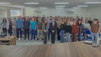 Banner horizontal com foto dos participantes da última etapa do Ciclo. Há várias pessoas, em pé, posicionadas lado a lado, em uma grande sala. Ao centro, os auditores Geovane Eziel e Vivan Savedra. 