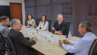 Banner horizontal com foto de seis autoridades reunidas diante de uma mesa enquanto conversam. Entre os presentes, o conselheiro Herneus De Nadal, o conselheiro substituto Gerson Sicca e a procuradora-geral do MPTC/SC, Cibelly Farias. 