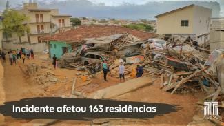 Foto de uma das áreas atingidas pelo rompimento do reservatório. Um amontoado de madeira onde deviam ser 2 casas. Algumas pessoas observam a cena. Na parte inferior em fundo marrom, com letras brancas, a frase ”Incidente afetou 163 residências”