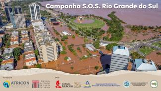 Banner horizontal. Imagem aérea de uma cidade alagada, com prédios e casas sobre a água. No canto superior direito da imagem, o texto "Campanha S.O.S Rio Grande do Sul". Na borda inferior, sobre tarja bege, logo dos realizadores, TCE/SC e Atricon, e apoiadores da campanha, IRB, Abracom, Audicon e ASTC.