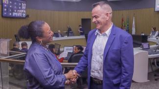 Foto da nova diretora da Ouvidoria, Walkiria Machado Rodrigues Maciel, à esquerda, cumprimentando o Servidor Paulo Salum, à direita, que era o diretor da unidade e se aposentou.     