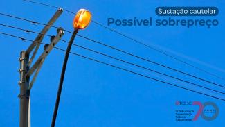 Banner horizontal com imagem, vista de baixo, de um poste de luz com o céu azul ao fundo. Sobre a foto, na lateral direita superior, na cor azul, o texto “Sustação cautelar. Possível sobrepreço”. No canto inferior direito, selo comemorativo aos 70 anos do TCE/SC.  
