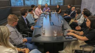 Foto que mostra 14 pessoas sentadas diante de uma mesa de reunião enquanto conversam, na sede do TCE/SC. Entre os presentes, integrantes da prefeitura de Florianópolis, do Todos pela Educação e do TCE/SC. Na ponta, o servidor Rafael Tachini e o diretor-geral de Controle Externo, Sidney Antônio Tavares Júnior. 