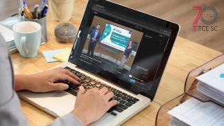 Banner horizontal com foto de mãos que digitam em um notebook sobre uma mesa de madeira, onde há canetas, papéis e uma xícara. Na tela, uma transmissão do TCE/SC que mostra os servidores Jean Rodrigues e Michelle Padovese fazendo a apresentação do PNTP. No canto superior direito da imagem, logo comemorativo aos 70 anos do TCE/SC. 