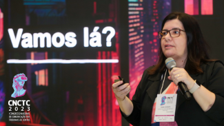 Foto de Tânia Vicente palestrando no auditório do TCE. Ela é morena e veste um blaser preto. Ao fundo, projeção da apresentação, onde aparece a frase "Vamos lá". No canto inferior esquerdo, a logo do Congresso.