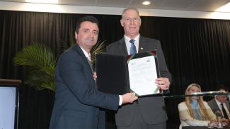 Foto do presidente do TCE/SC, conselheiro Herneus De Nadal, ao lado do presidente do IASC, Gilberto Lopes Teixeira, durante sessão solene. Eles seguram, juntos, e mostram para a foto um documento assinado. Ambos vestem terno e gravata.
