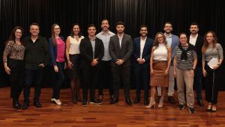 Foto com os organizadores do evento — servidores do Lince — e com os integrantes dos TCE/SC que apresentaram os desafios. Ao todo, há 13 pessoas, entre homens e mulheres, em pé, no palco do auditório, um ao lado do outro, enquanto olham para a foto. 