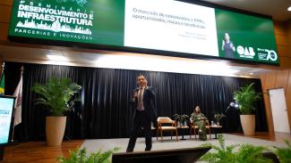 Banner horizontal com a imagem do diretor-presidente da Associação Brasileira de Concessionárias de Rodovias, Marco Aurélio de Barcelos Silva, durante palestra no Seminário Desenvolvimento e Infraestrutura. Ele é um homem branco, de cabelos escuros. Veste terno e gravata e está em pé, no palco do auditório do TCE/SC, enquanto fala ao público. Ao fundo, no telão, é projetada uma apresentação de slides e o logo do evento. 