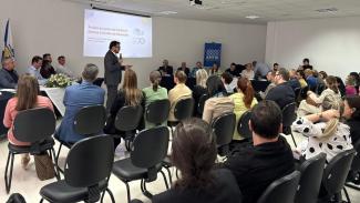Imagem mostra um grupo de pessoas observando, ao fundo, uma explanação de um homem que está em pé.