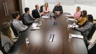 Descrição da imagem: Foto com os participantes da reunião, sentados em volta de uma mesa retangular. Ao fundo, o presidente do TCE/SC, conselheiro Herneus De Nadal. À direita dele, as representantes da Fecam. À esquerda dele, a chefe do Gabinete da Presidência, três servidores da DIE e uma servidora da DAP. Sobre a mesa, papéis, celulares, copos, xícaras e um notebook. 