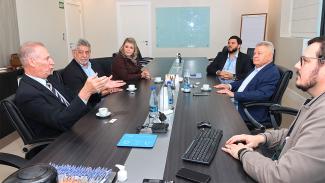 Foto dos participantes da reunião sentados diante de uma mesa enquanto conversam. Há seis pessoas. Entre os presentes, o presidente do TCE/SC, conselheiro Herneus De Nadal e o presidente do Conselho Deliberativo do hospital, Udo Dohler.