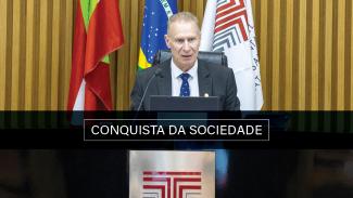 Foto colorida do presidente do TCE/SC, conselheiro Herneus De Nadal no Plenário, atrá dele as bandeiras de Santa Catarina, do Brasil e do TCE/SC ( da esquerda para a direita). Ao centro está escrito "Conquista da Sociedade". 