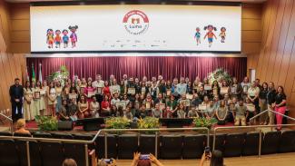 Banner horizontal com foto de várias pessoas no palco do auditório do TCE/SC. São os representantes das escolas premiadas pelo Prêmio Lume e autoridades, entre integrantes do TCE/SC, da educação do Estado e das demais instituições do acordo Lume. Alguns seguram certificados recebidos.