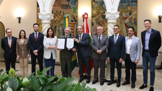 Foto de dez pessoas, em pé, uma ao lado da outra, durante a assinatura de protocolo de intenções relacionado à judicialização da Saúde. Na foto, entre homens e mulheres, estão o conselheiro Luiz Eduardo Cherem, do TCE/SC, o governador em exercício do Estado, desembargador João Henrique Blasi, que segura, juntamente com a secretaria da Saúde, Carmen Zanotto, e o ouvidor do Poder Judiciário, Osmar Nunes Júnior, o termo assinado. Eles mostram as folhas para a foto. Ao fundo, há pinturas nas paredes e colunas. 