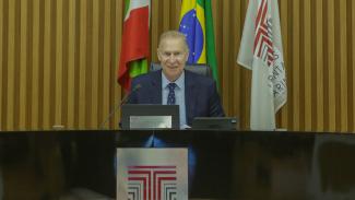 Foto do presidente do TCE/SC, conselheiro Herneus De Ndal, presidindo a Sessão plenária. Ele está sentado à mesa, com 3 bandeiras (de Santa Catarina, do Brasil e do TCE/SC) atrás dele.