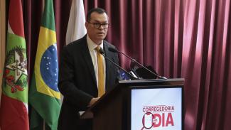 Banner horizontal com foto do conselheiro-corregedor do TCE/SC, Adircélio de Moraes Ferreira Júnior, no púlpito do auditório. Ele é um homem branco, de cabelos escuros. Veste terno e gravata e fala ao microfone. No púlpito, destaque para a logo do Corregedoria em Dia. Ao fundo, cortinas bordôs.   