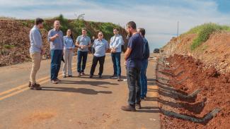Banner horizontal com foto de um grupo de pessoas reunido em uma rodovia durante visita técnica a uma obra de pavimentação. Os participantes estão posicionados sobre a pista. Nas laterais, há morros de terra. Na foto aparecem o presidente do TCE/SC, Herneus De Nadal; o diretor da DLC, Rogério Loch; auditores da área; o gestor do ACT, Moisés Hoegenn; e representantes da Amerios.