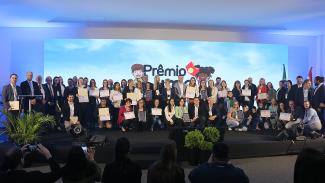 Imagem mostra todos os vencedores do Prêmio Lume no palco. Há cerca de 50 pessoas no palco. O fundo é azul.