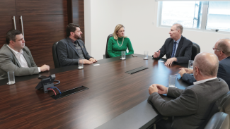 Imagem: na foto há seis pessoas ao redor de uma mesa marrom. São cinco homens e uma mulher, que veste uma blusa verde. Dois homens estão de costas. De frente aparecem o presidente do TCE/SC, conselheiro Herneus de Nadal, mais à direita da imagem, a chefe de gabinete Juliana Cardoso, o reitor Dilmar Baretta e o chefe de gabinete dele, Thiago Augusto. 