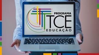 Foto de uma pessoa segurando um notebook com a tela virada para a foto. A foto está cortada, de modo que só é possível ver o tronco e os braços dela. Na tela, o logo do Programa TCE Educação, composto pelo nome e por sete lápis coloridos que formam a letra “T”, sobre fundo branco. Nas bordas laterais e inferior, há estreitos retângulos coloridos. 