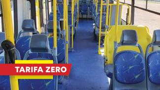 Imagem mostra o interior de um ônibus urbano. O chão e os bancos são azuis e as barras para as pessoas se segurarem são amarelas. À esquerda, no canto inferior, escrita em branco sobre uma tarja vermelha, há a expressão “tarifa zero”